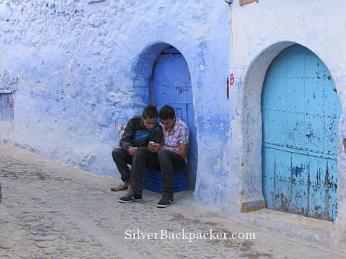 Chefchaouen teenagers sitting on blue crate texting